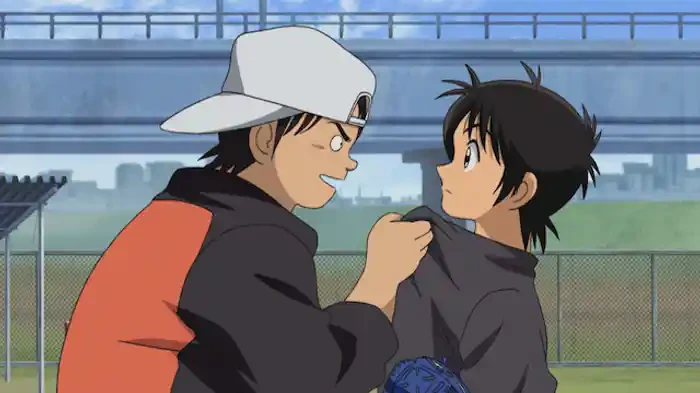 Two boys in baseball clothes talk beside a fenced school field.