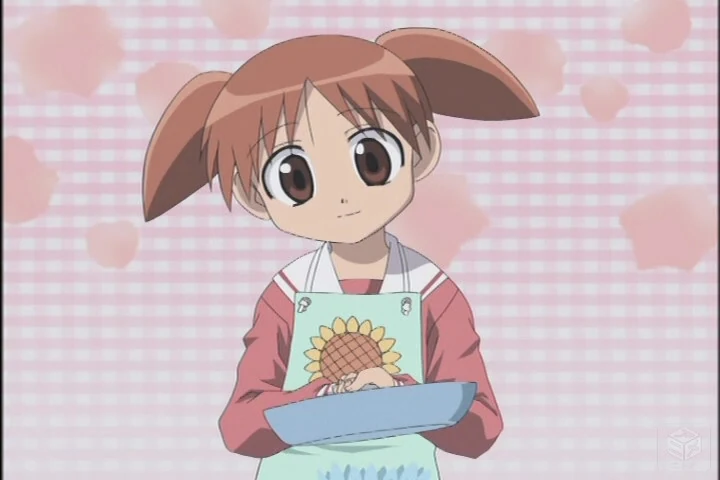 Chiyo wears a sunflower apron against a pink, heart-patterned background.