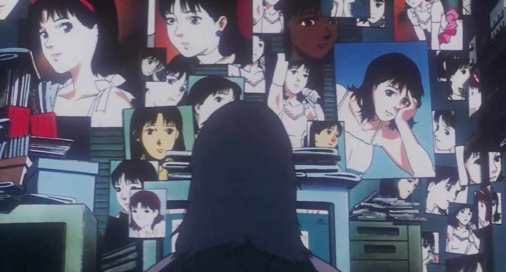 An unidentified seated figure faces a computer beneath a wall crowded with photographs and posters of Mima.