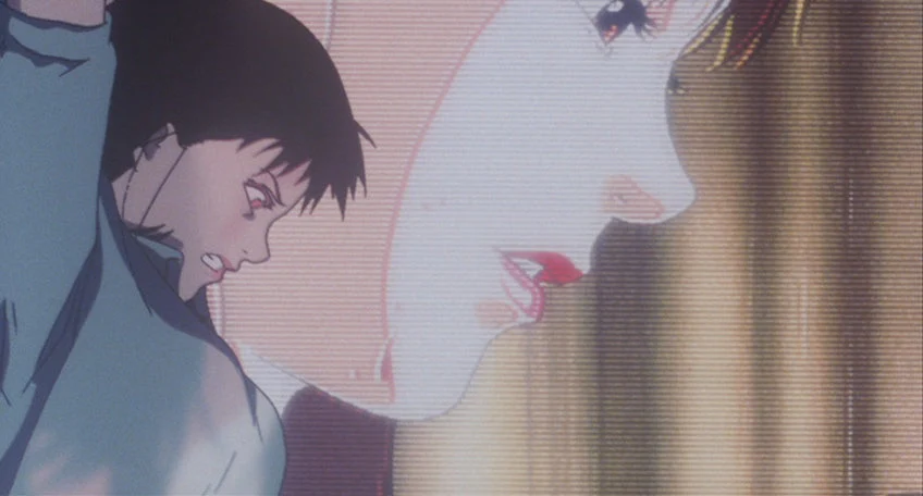 A woman's face fills a bright television screen while another dark-haired figure leans forward beside it.