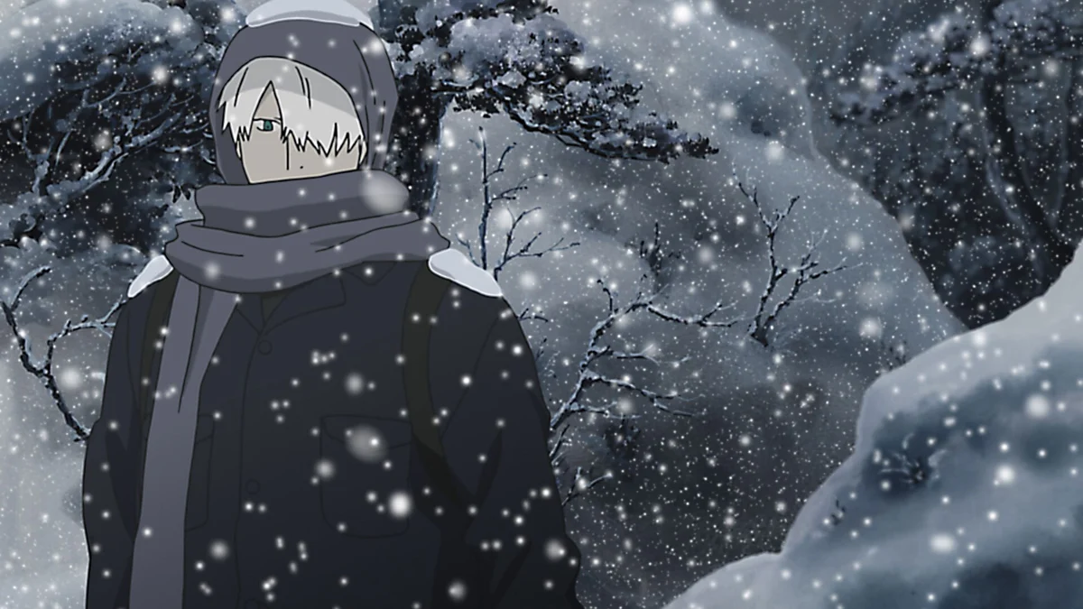 Ginko stands wrapped in a dark coat and scarf among snow-covered branches and falling snow.