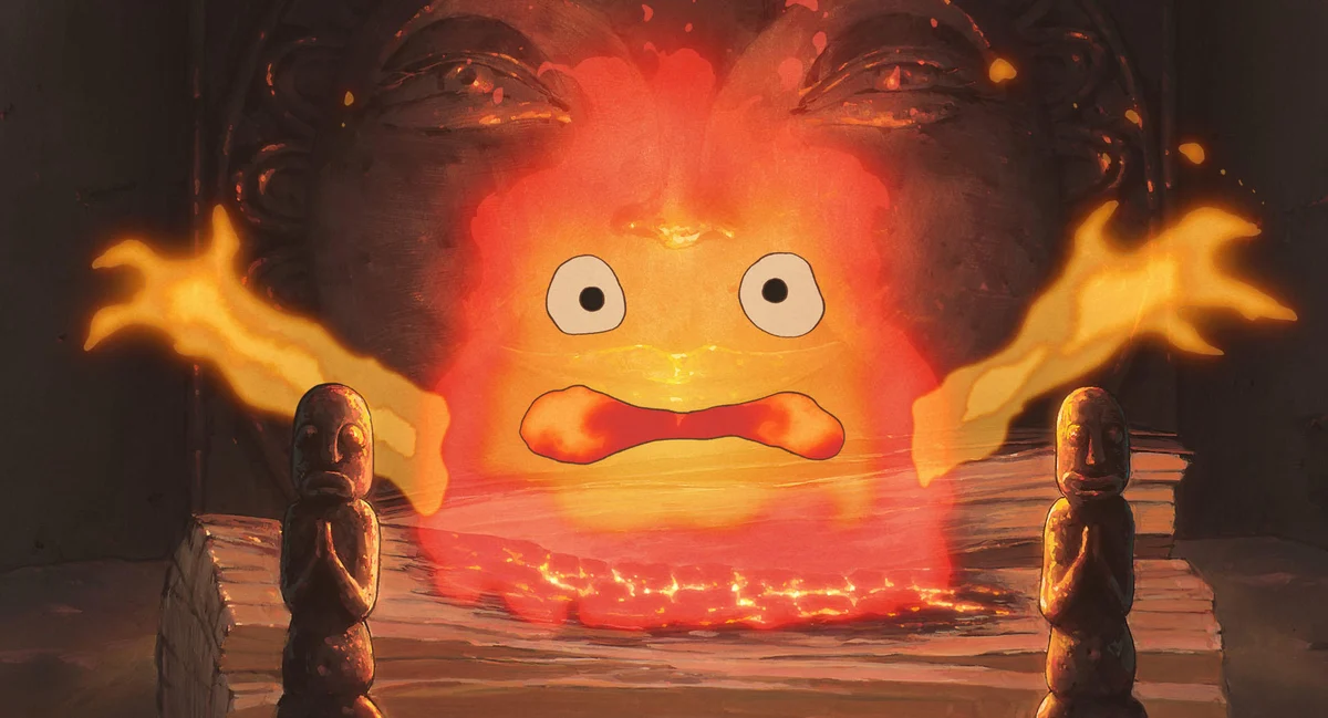 Calcifer’s wide-eyed orange flame fills the castle hearth between two dark metal supports.