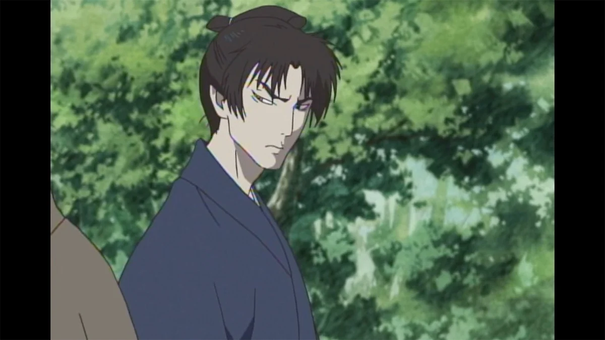 A dark-haired man in a blue robe stands in front of green foliage.