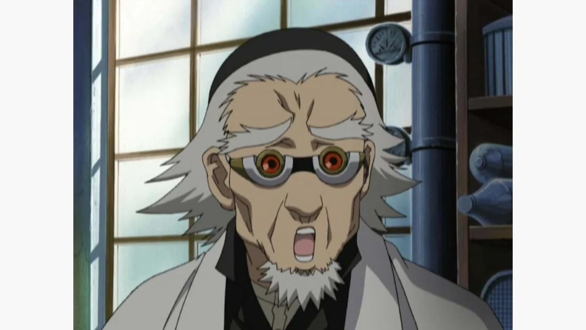 An older white-haired man wearing unusual round goggles speaks beside a tall window in a workshop.