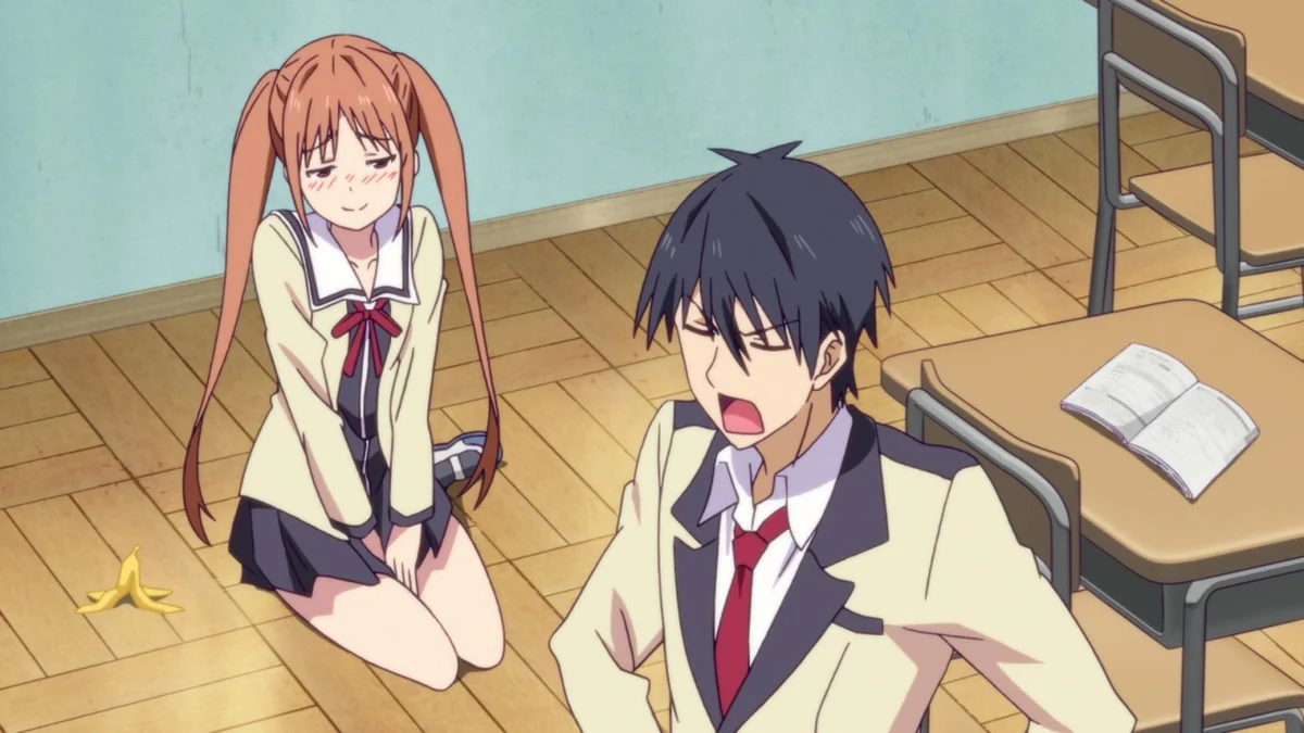 A schoolgirl kneels on a classroom floor beside a banana peel while a dark-haired boy looks exasperated near a desk and open book.