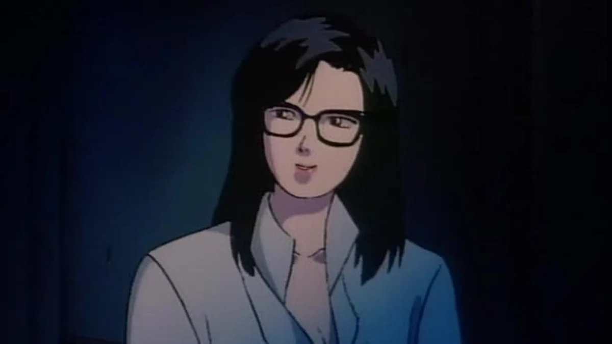 A long-haired woman wearing glasses and a pale laboratory coat looks to one side in a dark room.