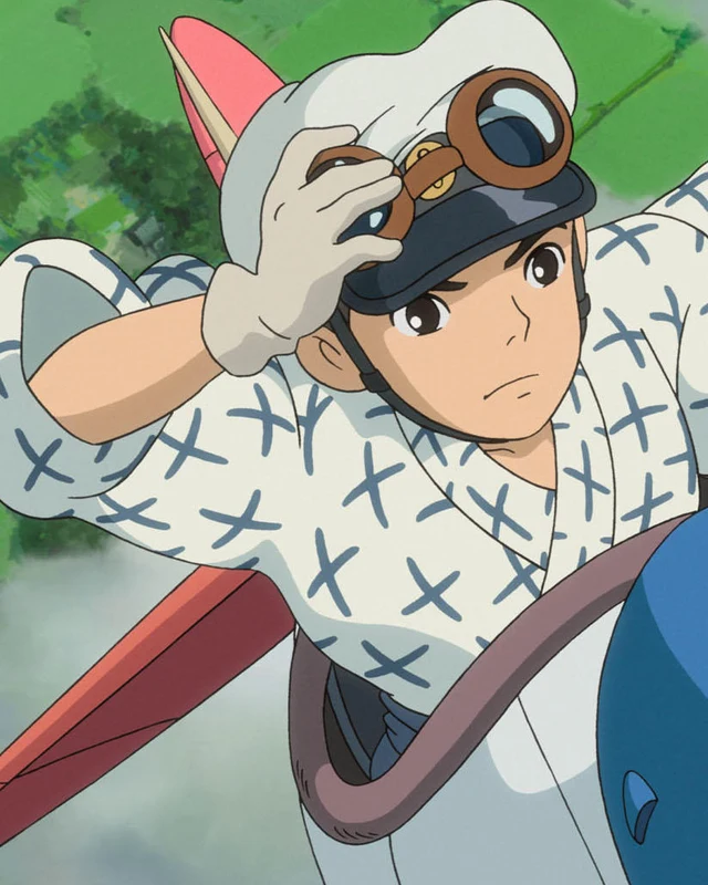 A young Jiro in flying goggles raises a gloved hand beside an aircraft.