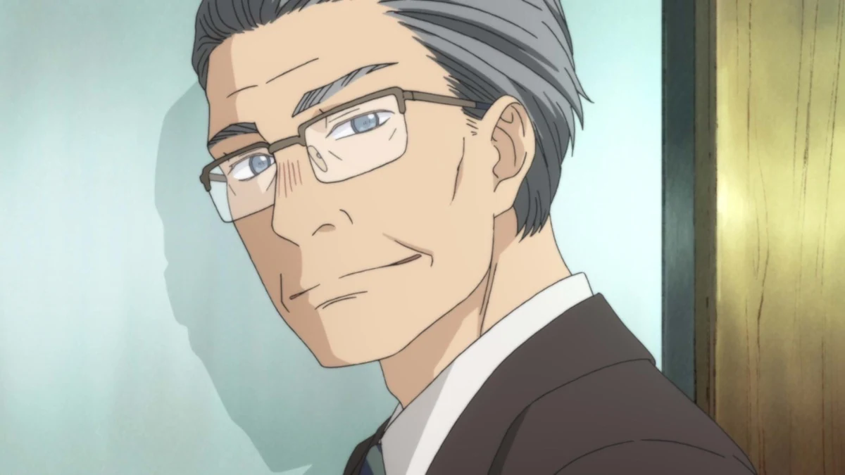 A bespectacled man in a suit turns his head against a wooden background.