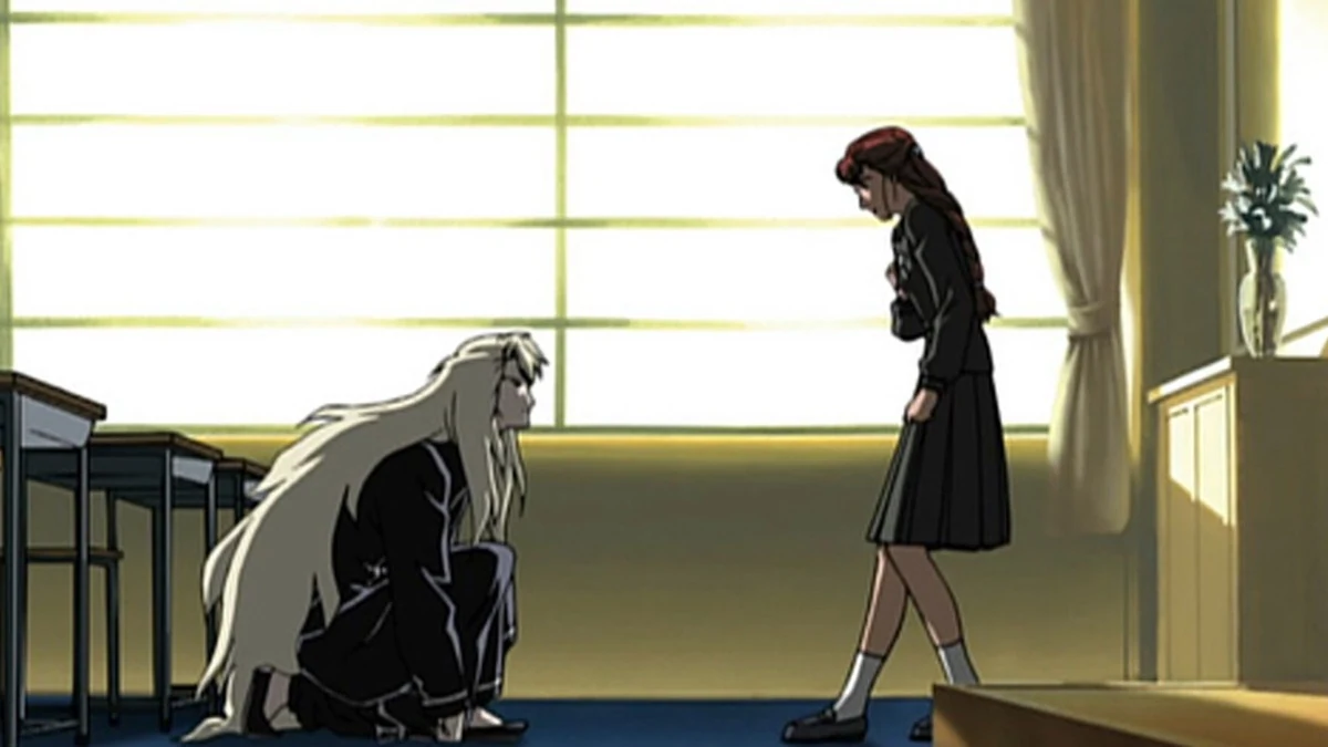A long-haired man kneels before a red-haired schoolgirl in a classroom.