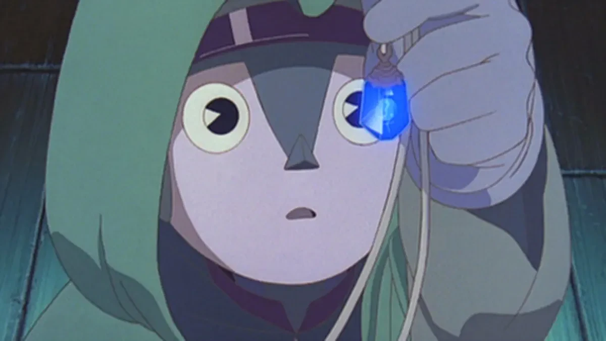 A pale puppet face watches a small blue object held near one eye.