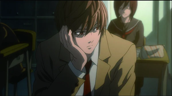 Light rests his cheek on one hand at a classroom desk, wearing a tan school blazer, with a classmate behind him.
