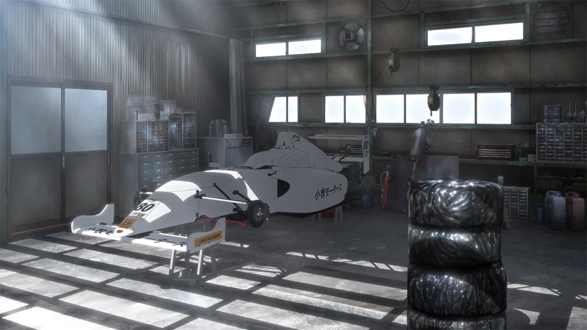 Komaki Motors' white number 80 racing car sits on stands in a sunlit workshop beside stacked tyres.