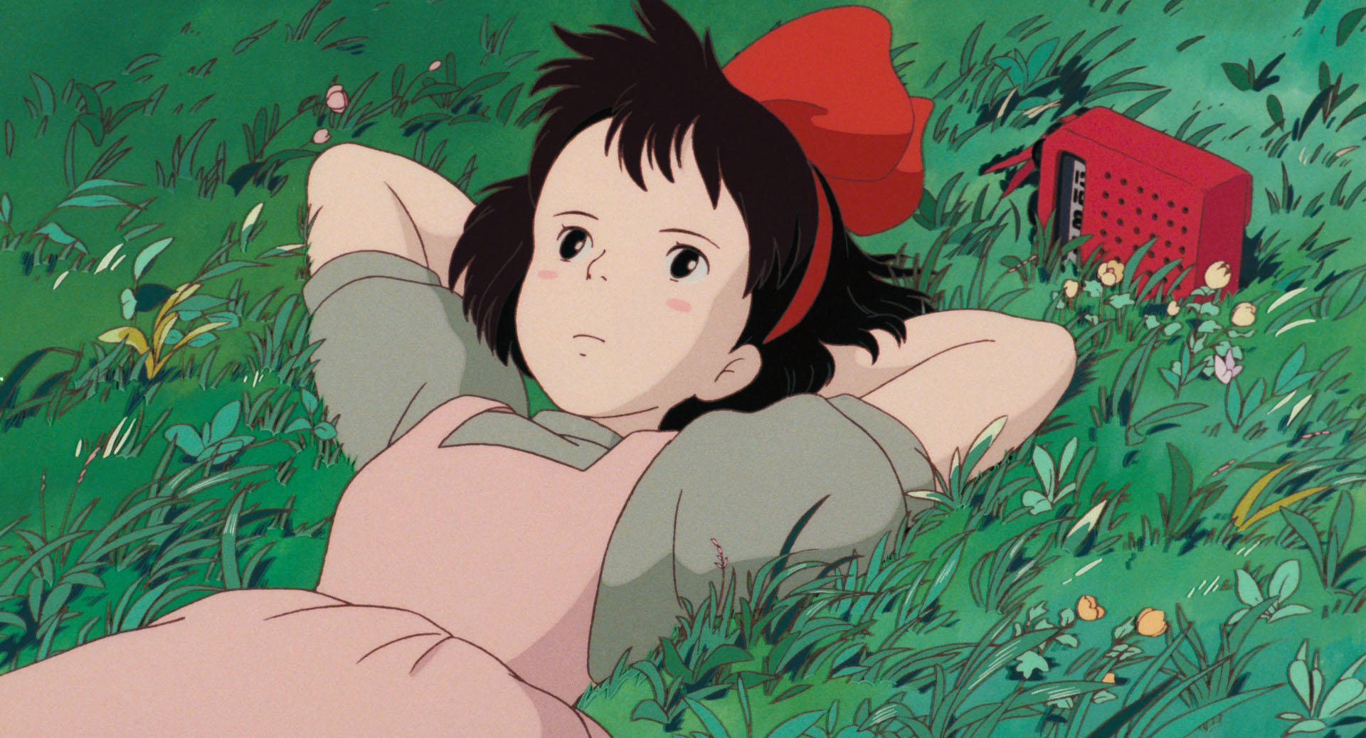 Kiki rests in the grass with her red bow.