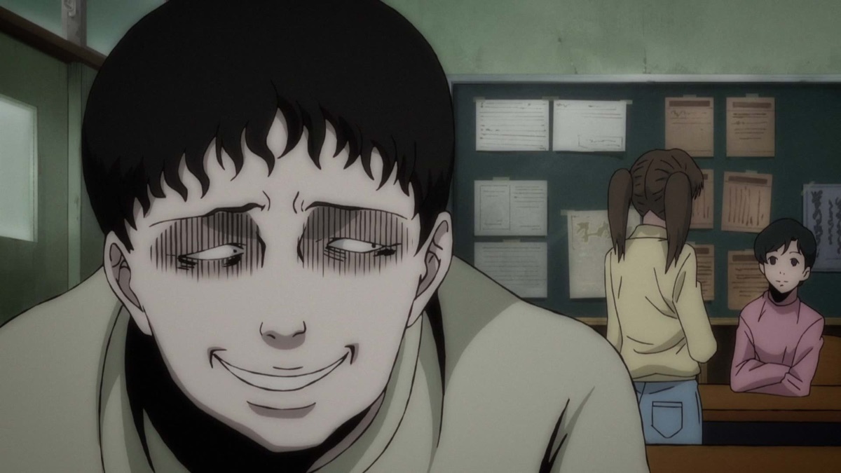 A dark-haired boy leans towards the viewer in a classroom, with two other people behind him.
