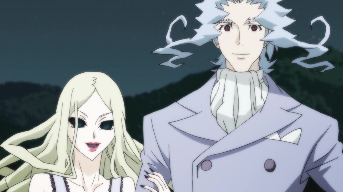 A formally dressed pale-haired man stands beside a fair-haired woman outdoors at night.