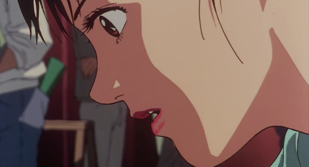 Close view of a woman's eye, cheek and slightly open mouth, with figures blurred behind her.