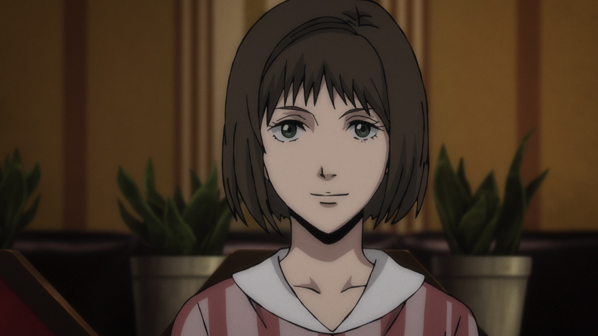 A short-haired young woman faces forwards in a wood-panelled room with plants behind her.