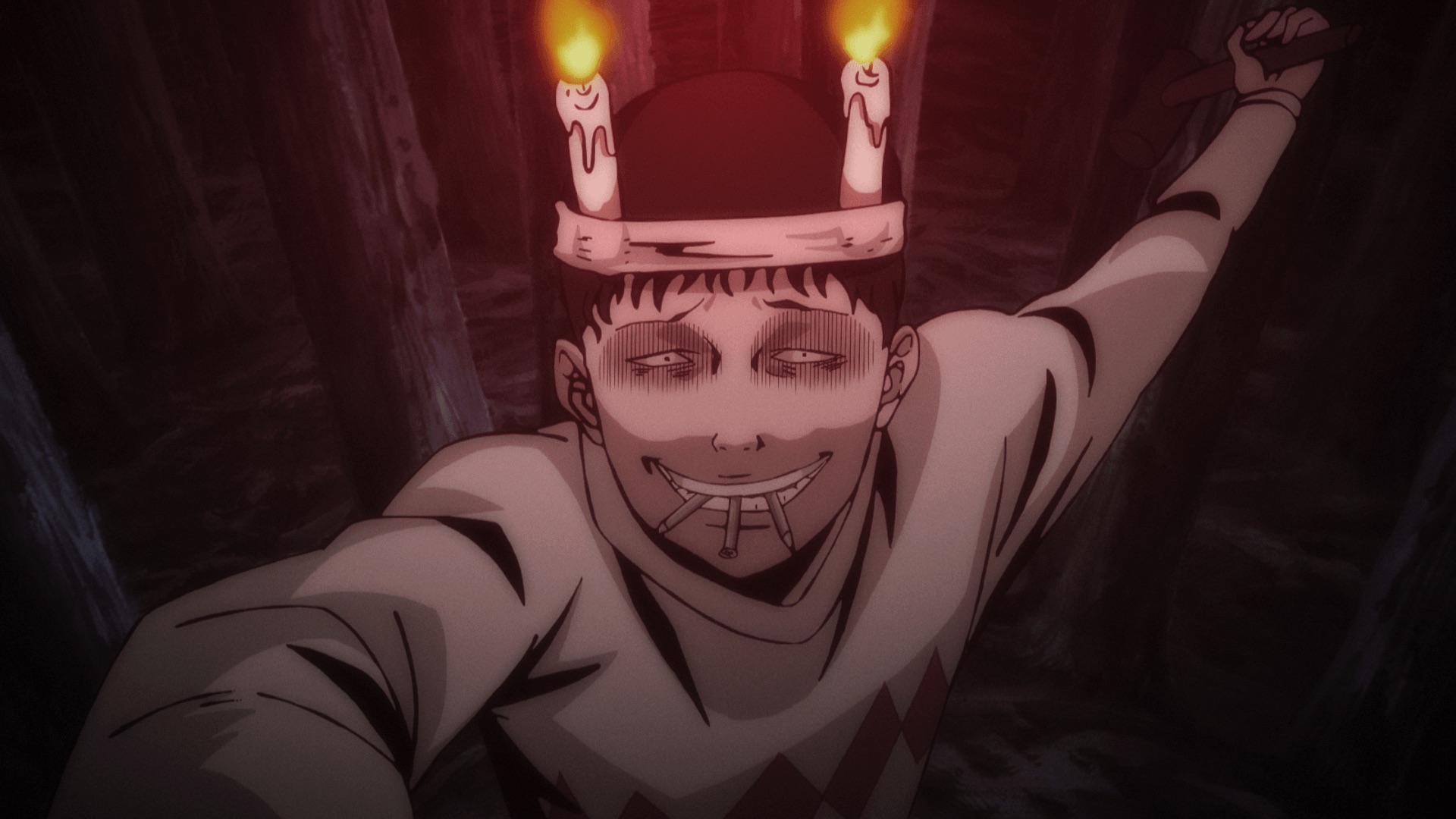 Souichi holds several nails in his mouth beneath two lit candles, with a hammer raised among trees.
