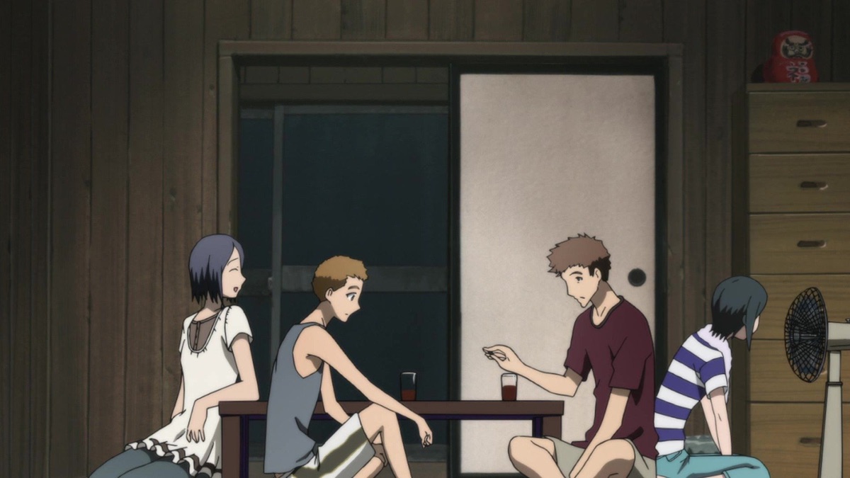 Four young villagers gather around a low table in a wooden room with drinks and an electric fan.