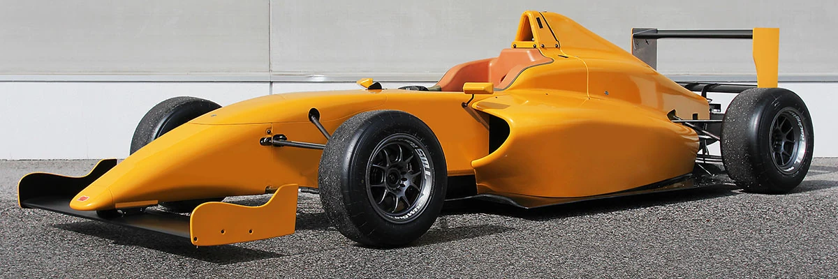 An orange Dome F110 single-seater, photographed from the front and side, with its wheels and suspension exposed.