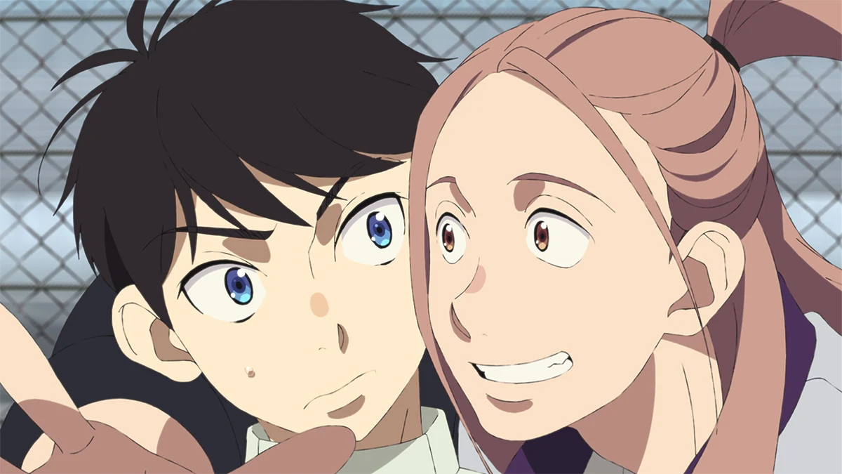Haruka and Kotarou stand close together beside a trackside fence.