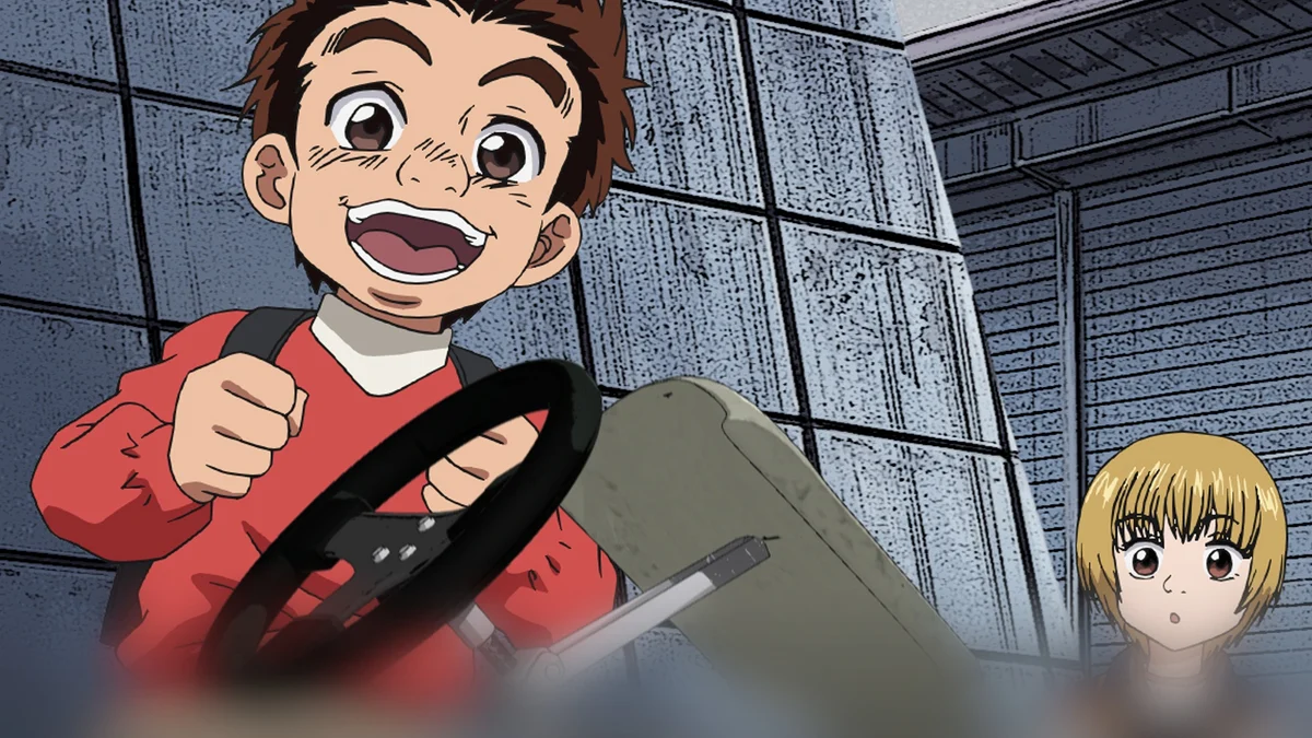 Capeta smiles as he holds a steering wheel, with a blond child looking on beside him.