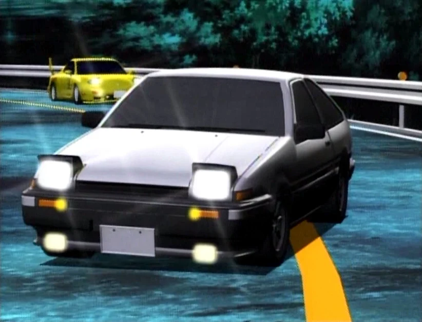 The white-and-black Toyota AE86 leads a yellow sports car around a mountain-road bend at night.