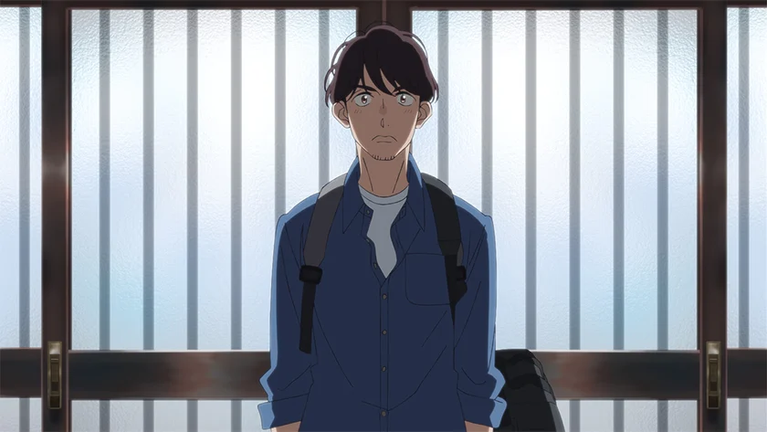 Kouya stands with a camera bag on his shoulder, framed by the bars of a bright window.