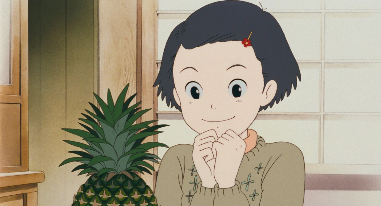 Young Taeko clasps her hands beneath her chin, smiling beside a fresh pineapple.