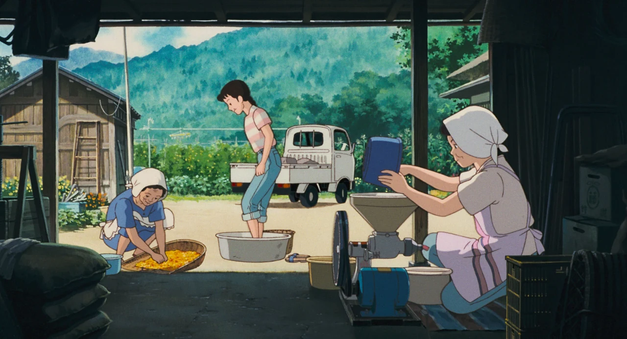 Taeko stands barefoot in a tub while two women process safflowers beside baskets and a machine in an open farm building.